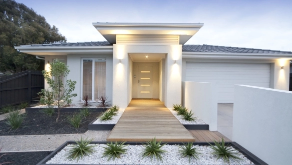 Biely moderný rodinný dom s dreveným chodníkom a rozsvieteným nástenným vonkajším osvetlením